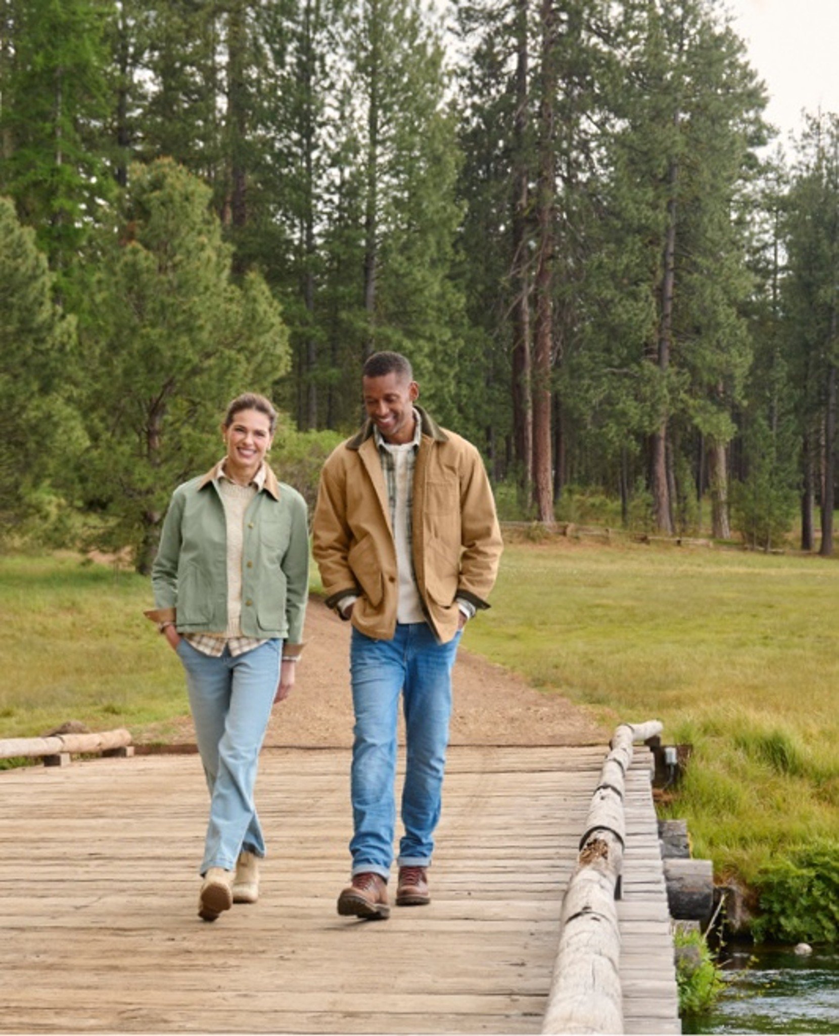 Two people in jackets and jeans walk on forest path.