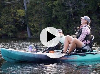 MacKenzie in a kayak holding a fish next to her instructor who is also in a kayak.