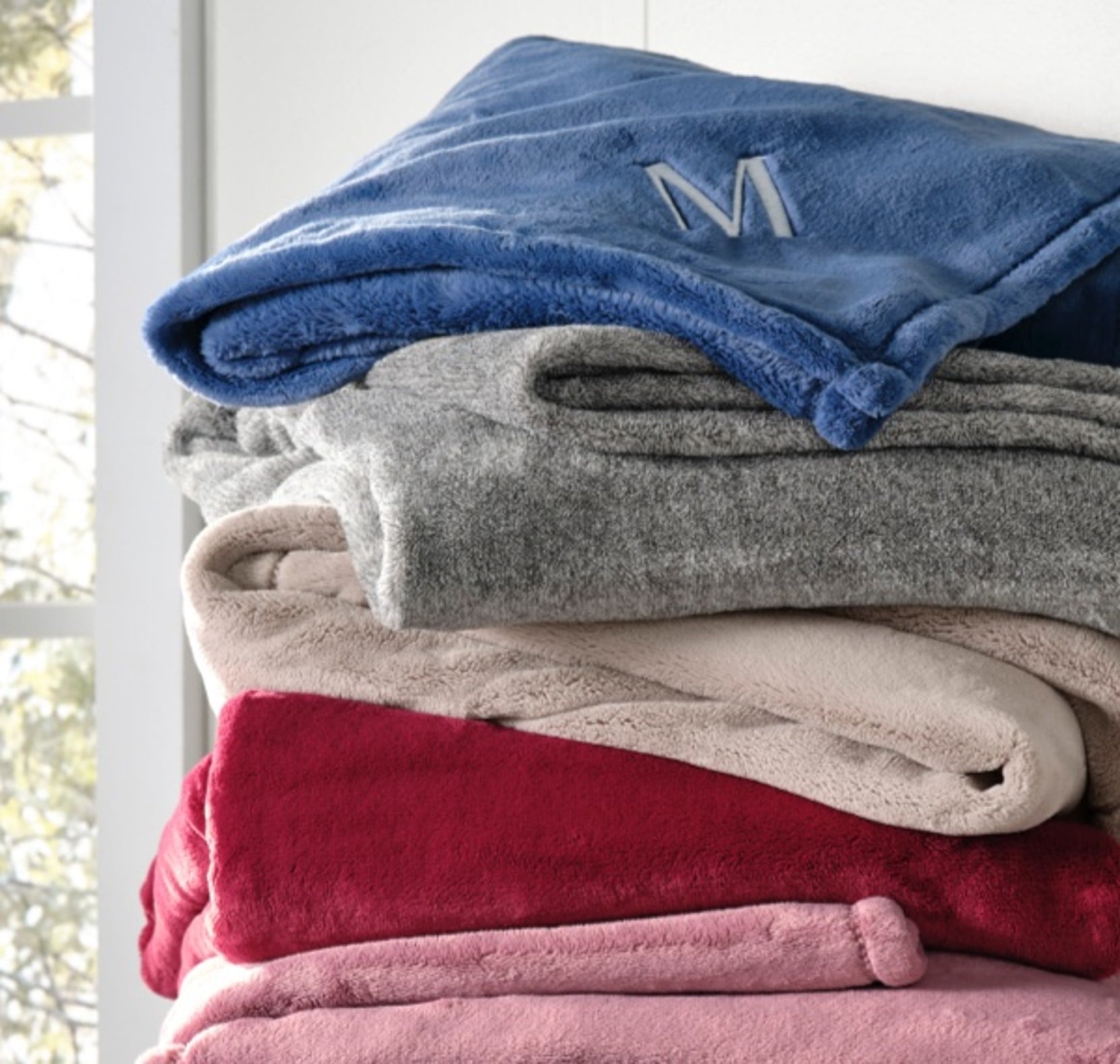 Folded plush throws in red, pink, gray, beige, and blue stacked neatly.