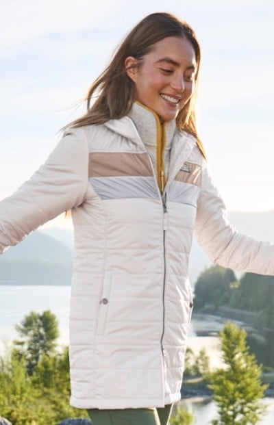 A woman wearing a long, white quilted jacket with horizontal beige and gray stripes on the chest.