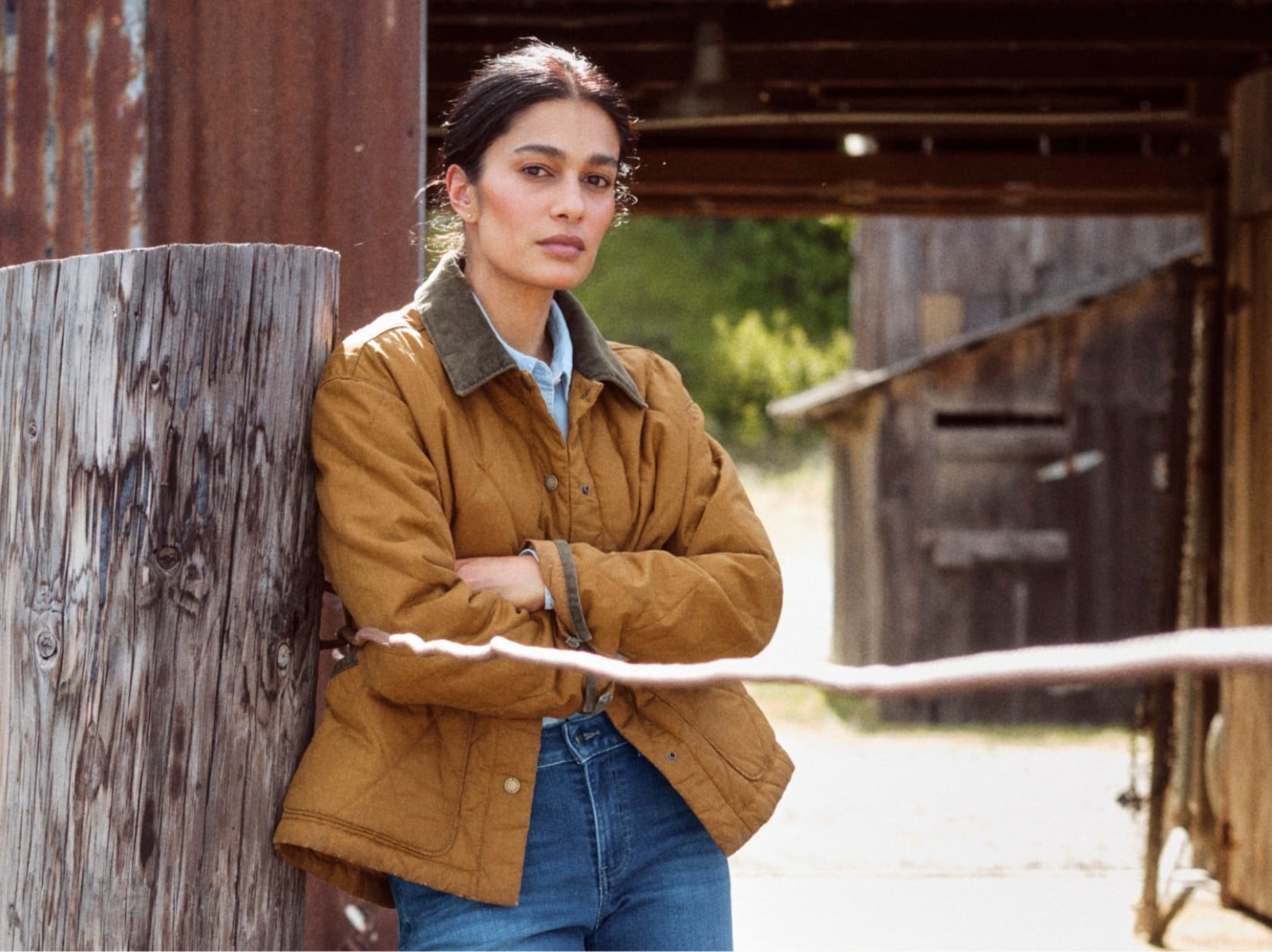 Woman wearing a brown field coat with a corduroy collar, standing near a rustic barn.