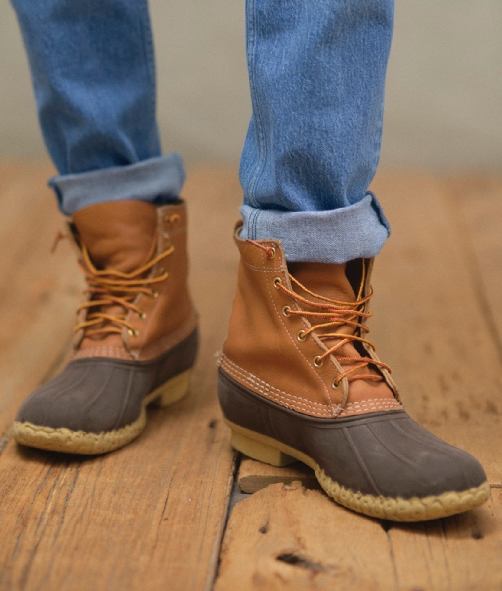 Close up of tan and brown L L Bean Boots with rolled-up light blue jeans.