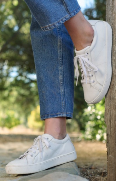 Image depicting a woman wearing sneakers standing on a rock with one foot on a fence post.