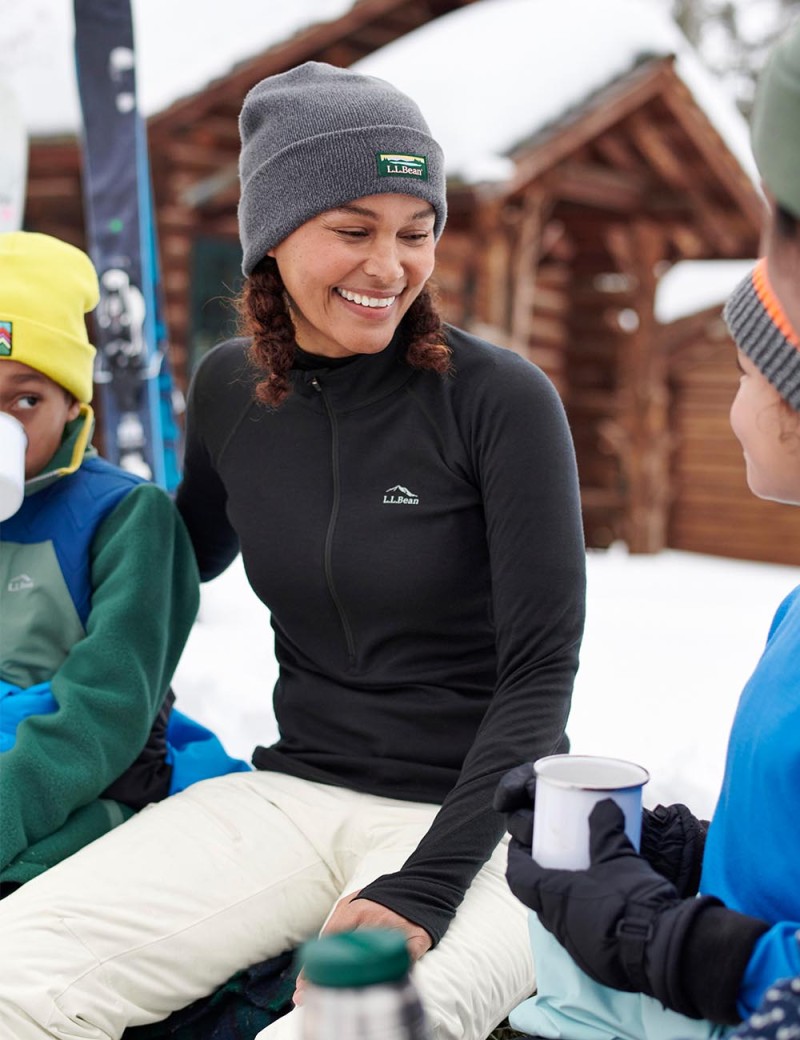 A women in an L.L.Bean heavyweight base layer and knit cap sitting by a fire.