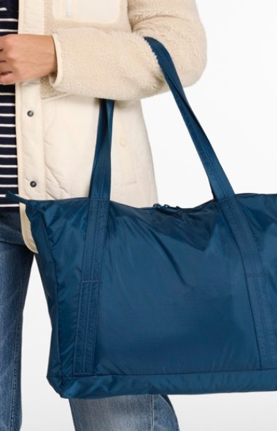 Navy tote bag with long straps carried by someone wearing a light jacket and striped shirt, shown against a plain backdrop.