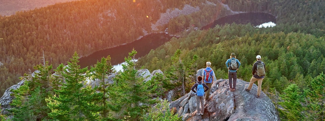 4 people standing on top of a mountain watching the sun set.