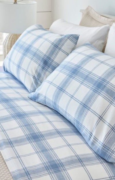 A neatly folded bed with blue and white plaid bedding and pillows.