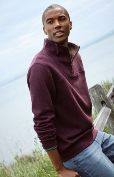 Person in a burgundy quarter-zip pullover posing outdoors on a grassy hillside.