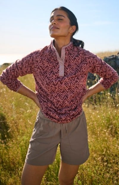 Person standing in a grassy field wearing a patterned pullover and hiking shorts.