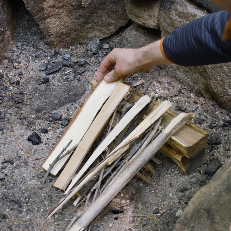 Nate adding tinder to the first layer of logs, filling the gaps between logs.