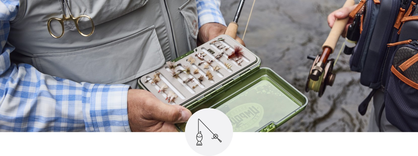 Fisherman holding a fly box with fly fishing flies with water in the background.