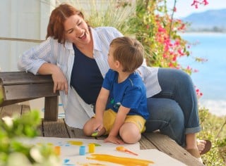 Mother and child sitting outside talking, the child's painting project on the ground beside them.