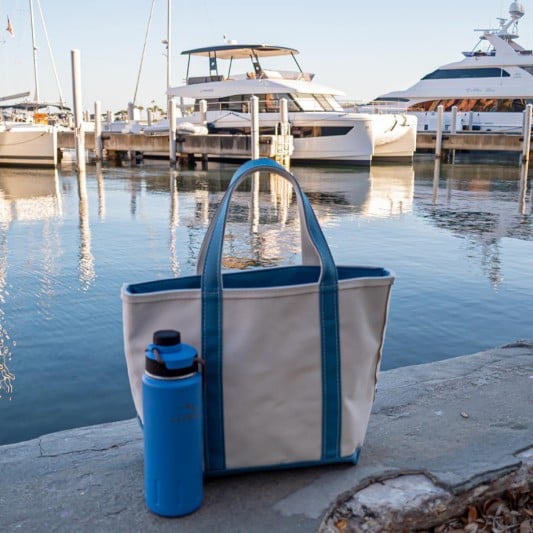 A Boat & Tote and water bottle on the dock, water and boats in the background.