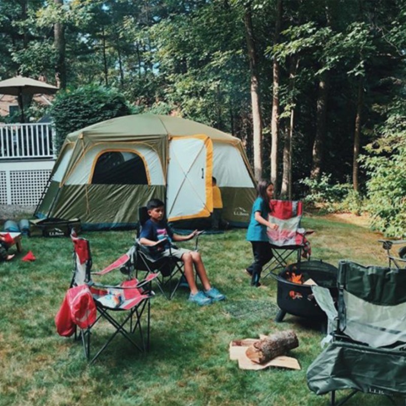 Tent and chairs set up in a back yard, children sit by a fire.