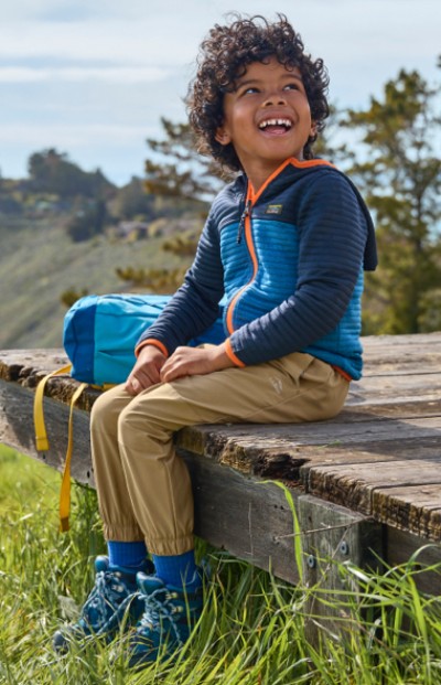 A child is sitting on a wooden bench outdoors, enjoying a peaceful moment with a forest landscape in the background.