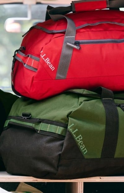 Cropped image of two L.L.Bean duffel bags, one red and one green, are stacked on a shelf.