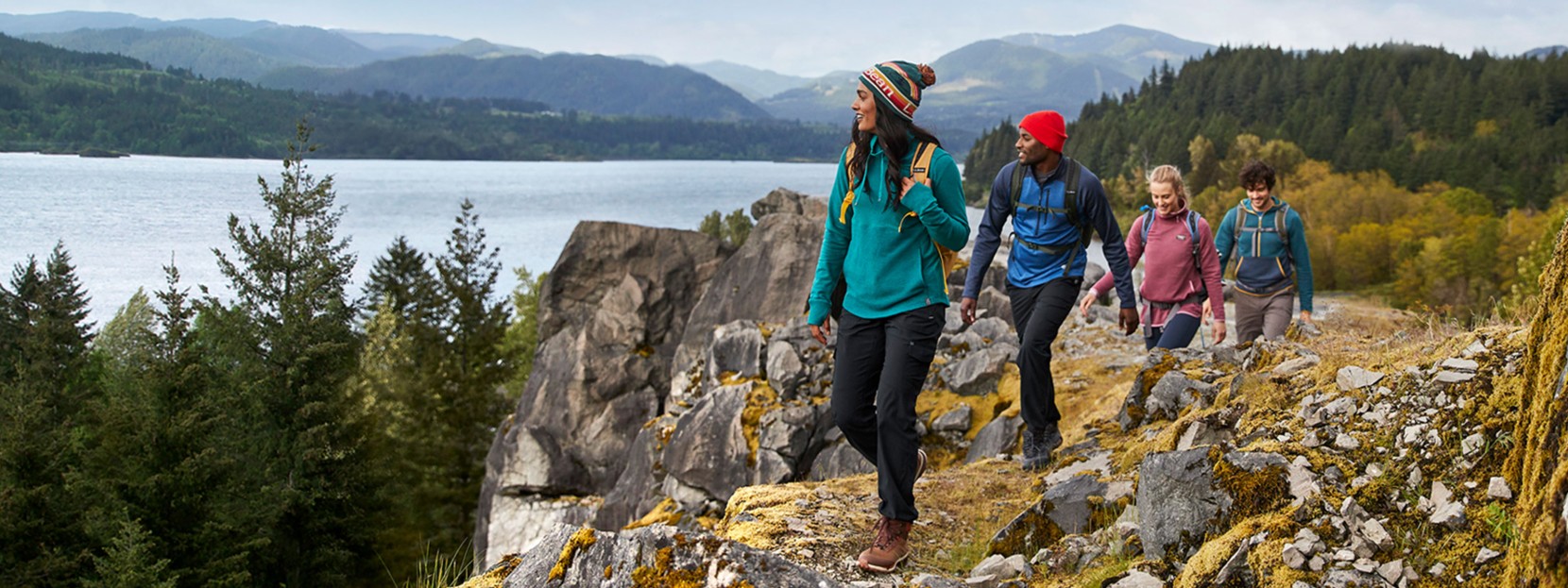 A group of four hikers walking along a lake with mountains in the background.