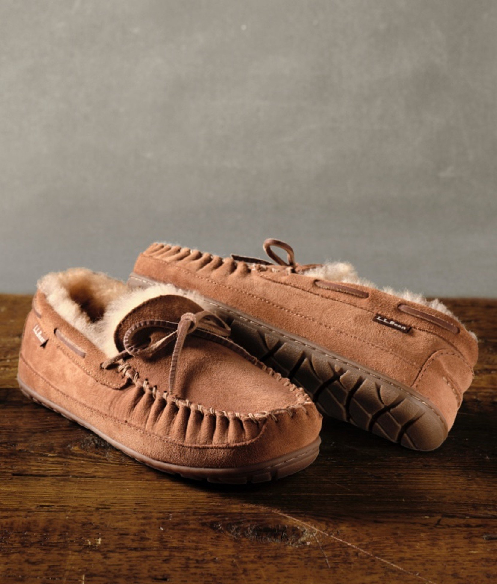 Tan moccasin slippers for men on a wooden surface.