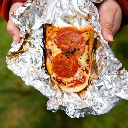 Hands holding french bread pepperoni pizza in alumninum foil.