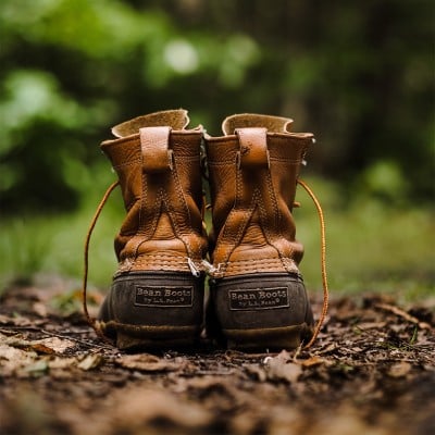 Rear view of worn brown duck boots on a forest path.