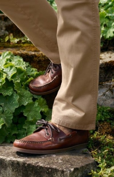 Close up image of person in brown leather moccasins and khaki pants on stone steps surrounded by green foliage.