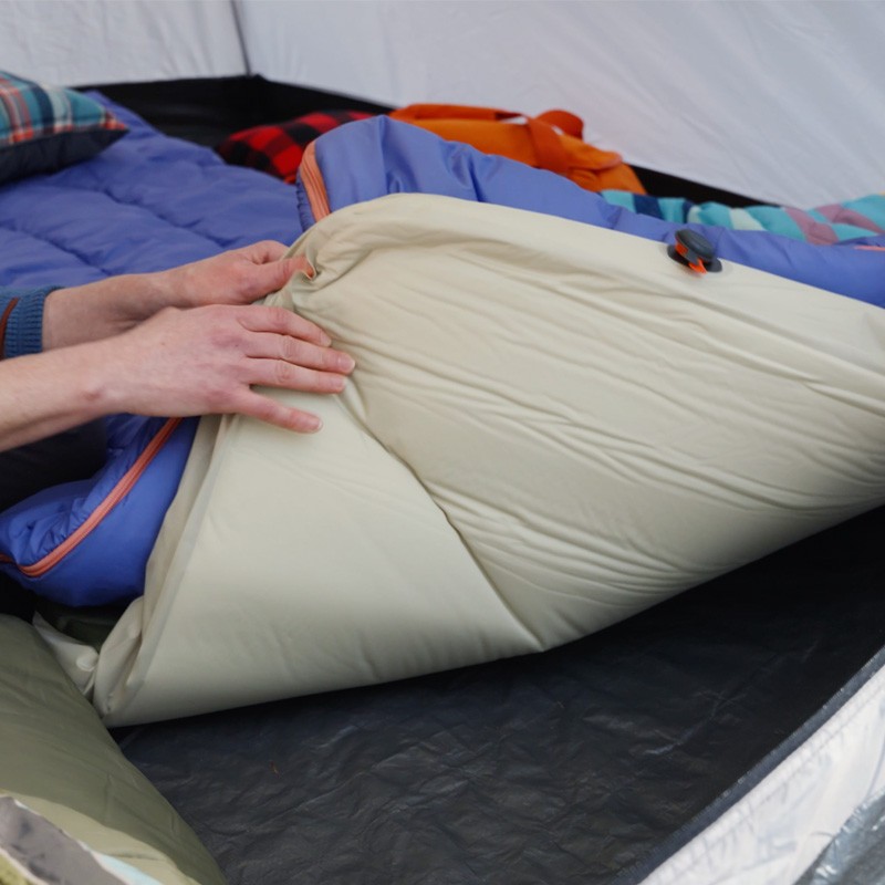 A person holding a blue L L Bean cooler by the lid, ready for an outdoor adventure. A person inside a tent inspects a L L Bean sleeping pad.