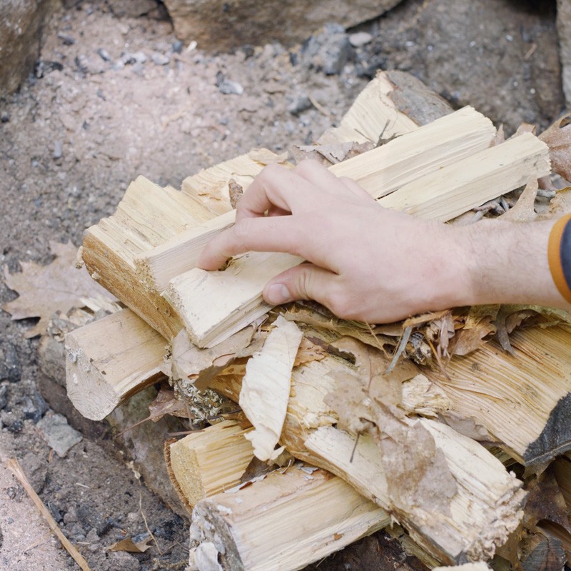 Nate adding tinder to the first layer of logs, filling the gaps between logs.