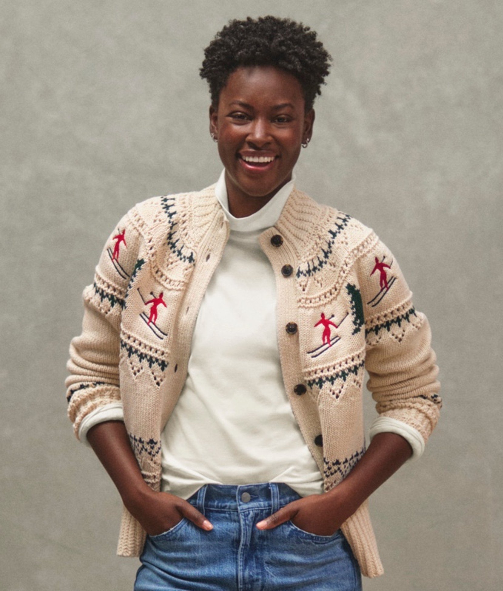 Woman in cream cardigan with festive embroidery, hands on hips.