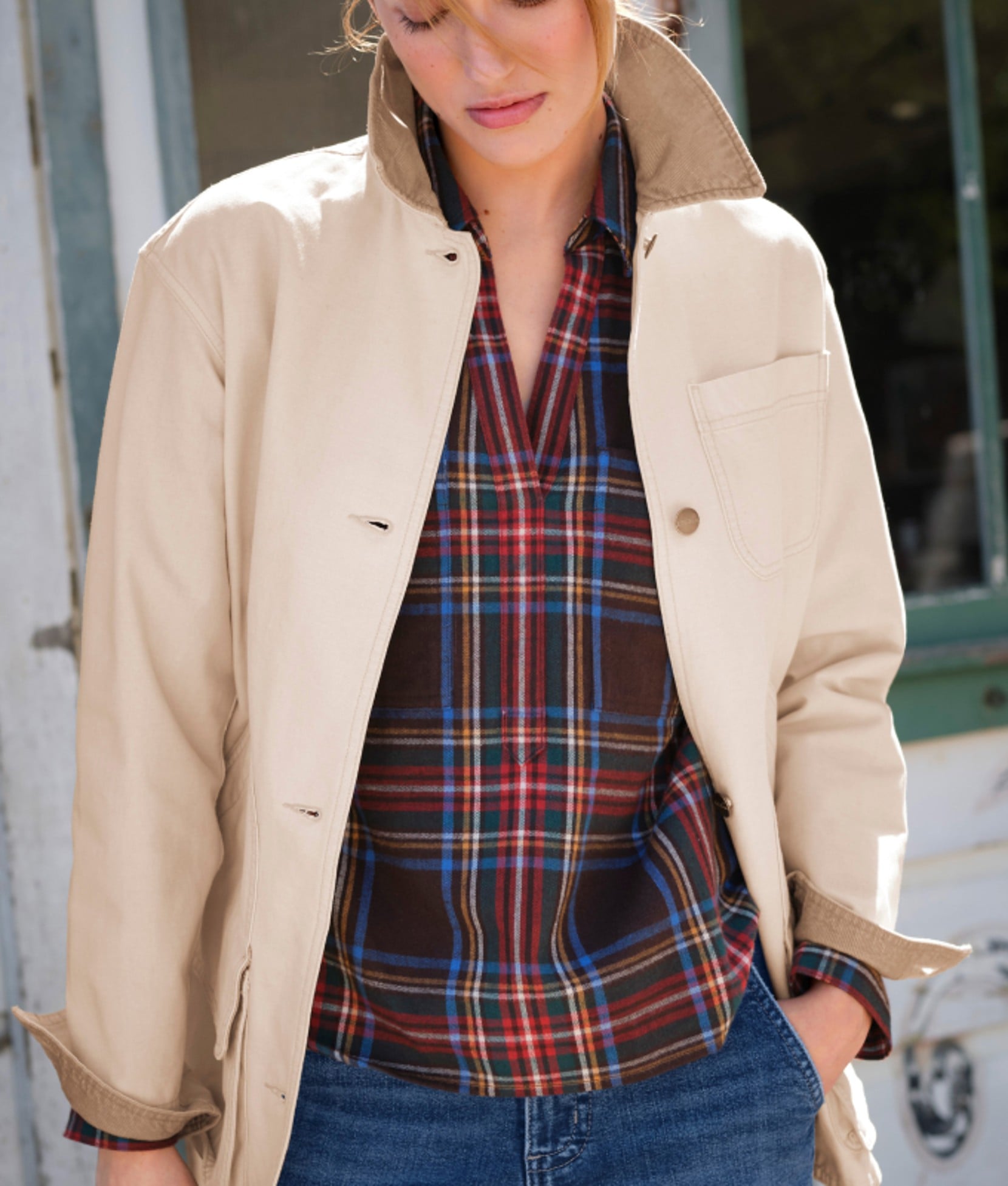 Woman wearing a cream field jacket layered over a plaid shirt.