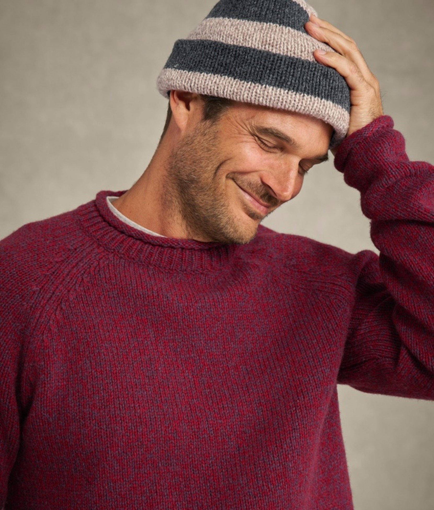 Man in maroon sweater adjusting a gray beanie.