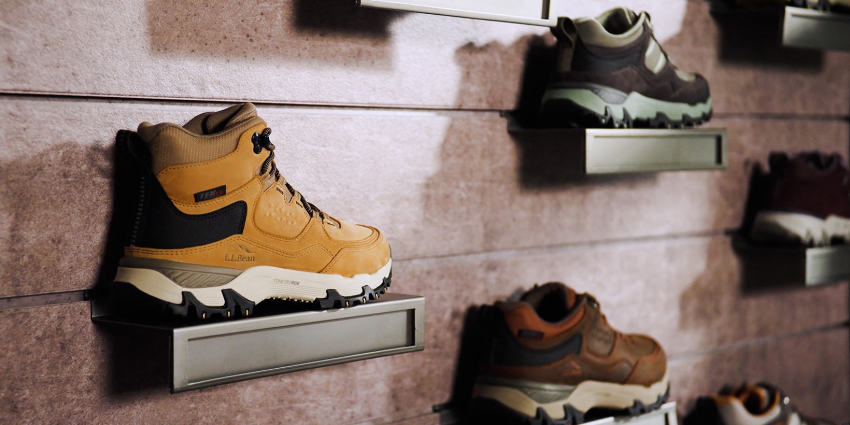 Various hiking boots on wall shelves, with a tan L L Bean boot prominently displayed in the foreground.