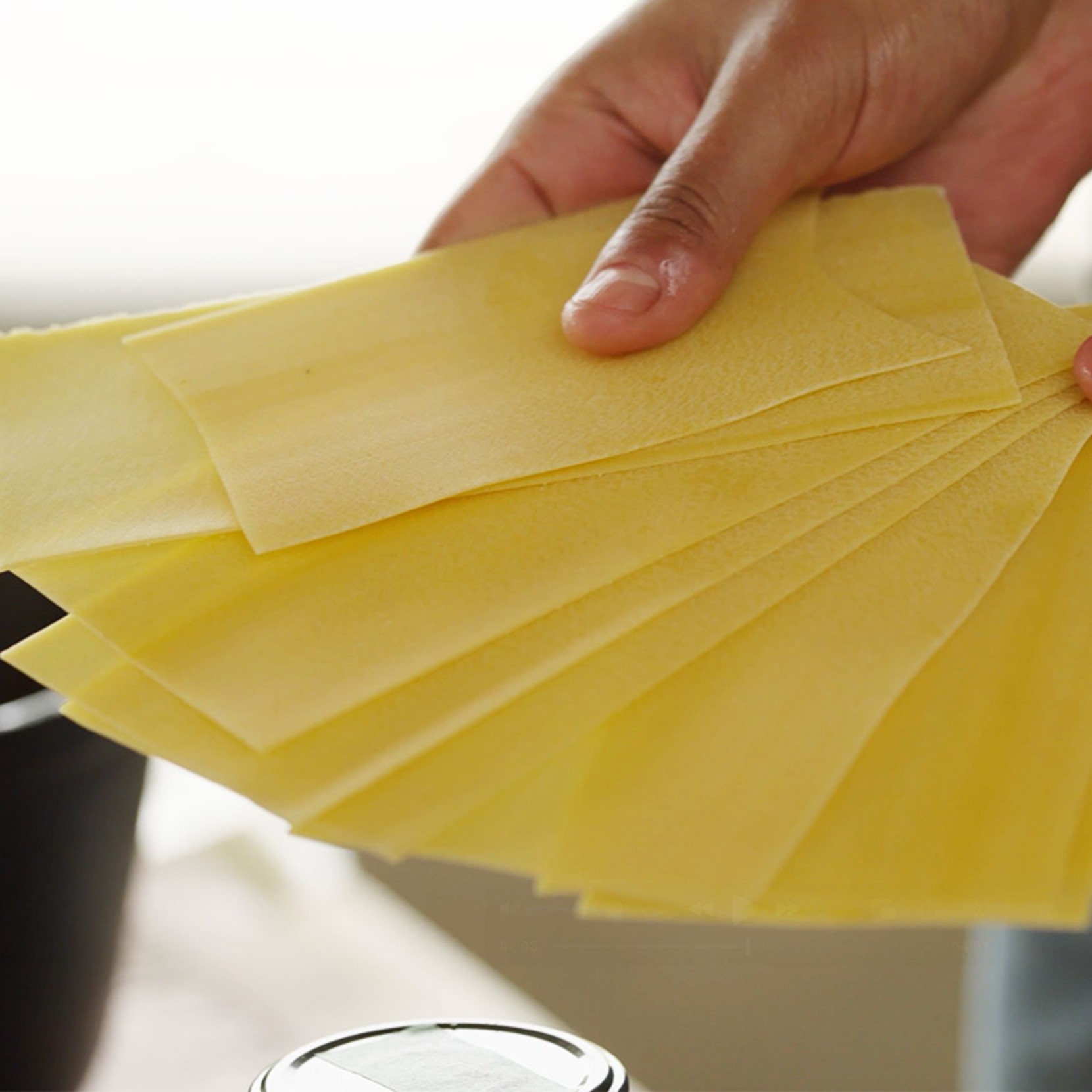 A hand holds several yellow lasagna pasta sheets fanned out.