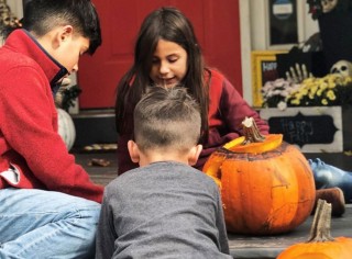 3 kids playing among jack-o-lanterns on a front porch.