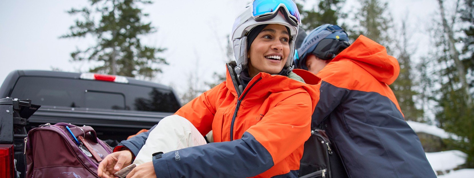 A couple getting their ski gear on at the back of a truck.