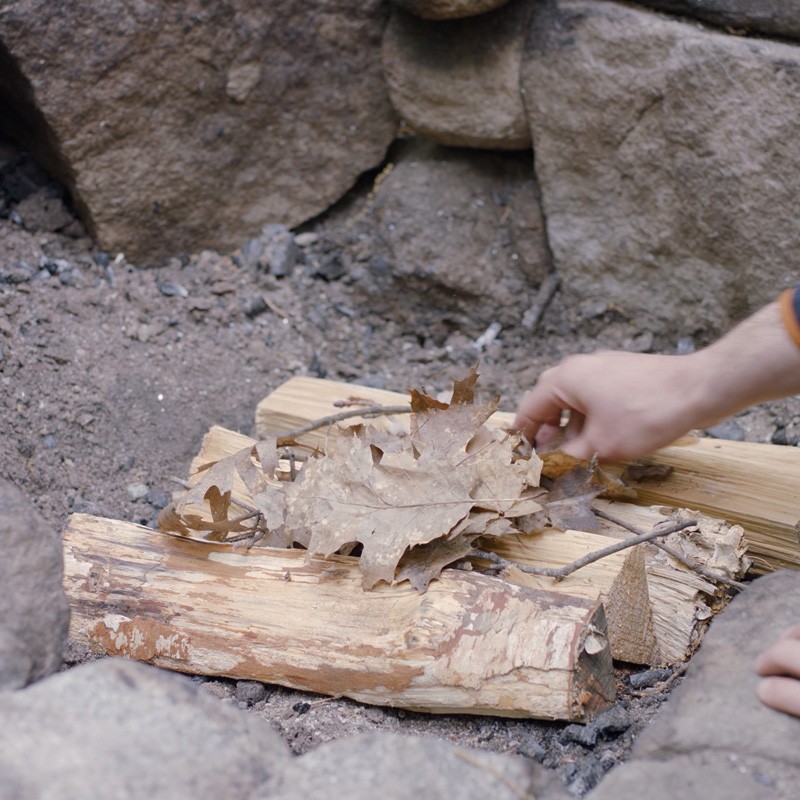 Nate adding tinder to the first layer of logs, filling the gaps between logs.