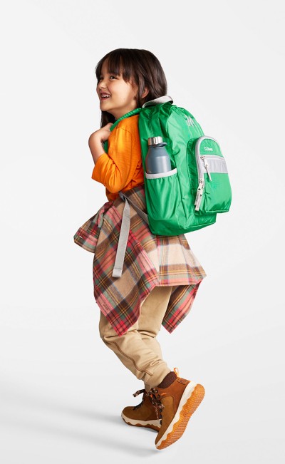 A young child from slightly behind, wearing a green Junior Original Book Pack.