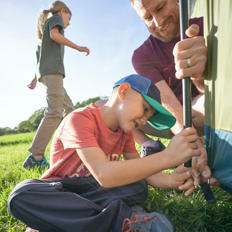 A man and child set up a tent, a girl walks by in the background.