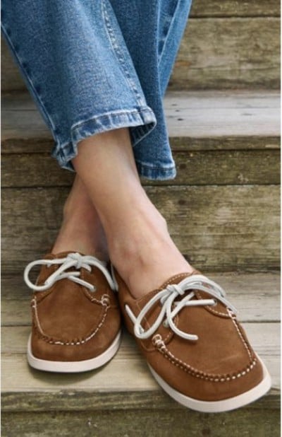 Close up of a person wearing brown boat shoes with white laces on wooden steps.