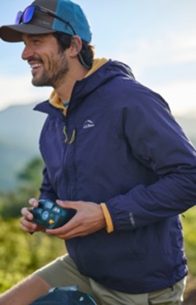 A man wearing a blue jacket and cap is holding a camera outdoors with a natural background.