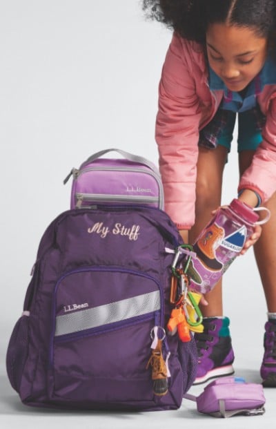 A child with a purple L L Bean backpack and sneakers, packing a water bottle, ready for school.