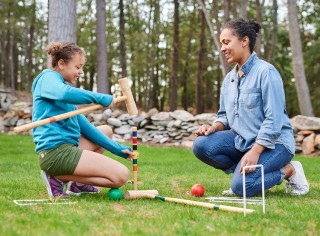 Mom an daughter kneeling down in green grass, setting up an L.L.Bean croquet set.