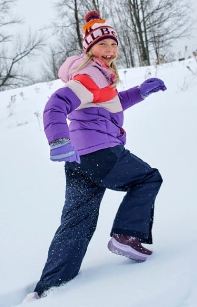 Child playing in deep snow while wearing a colorful winter outfit.