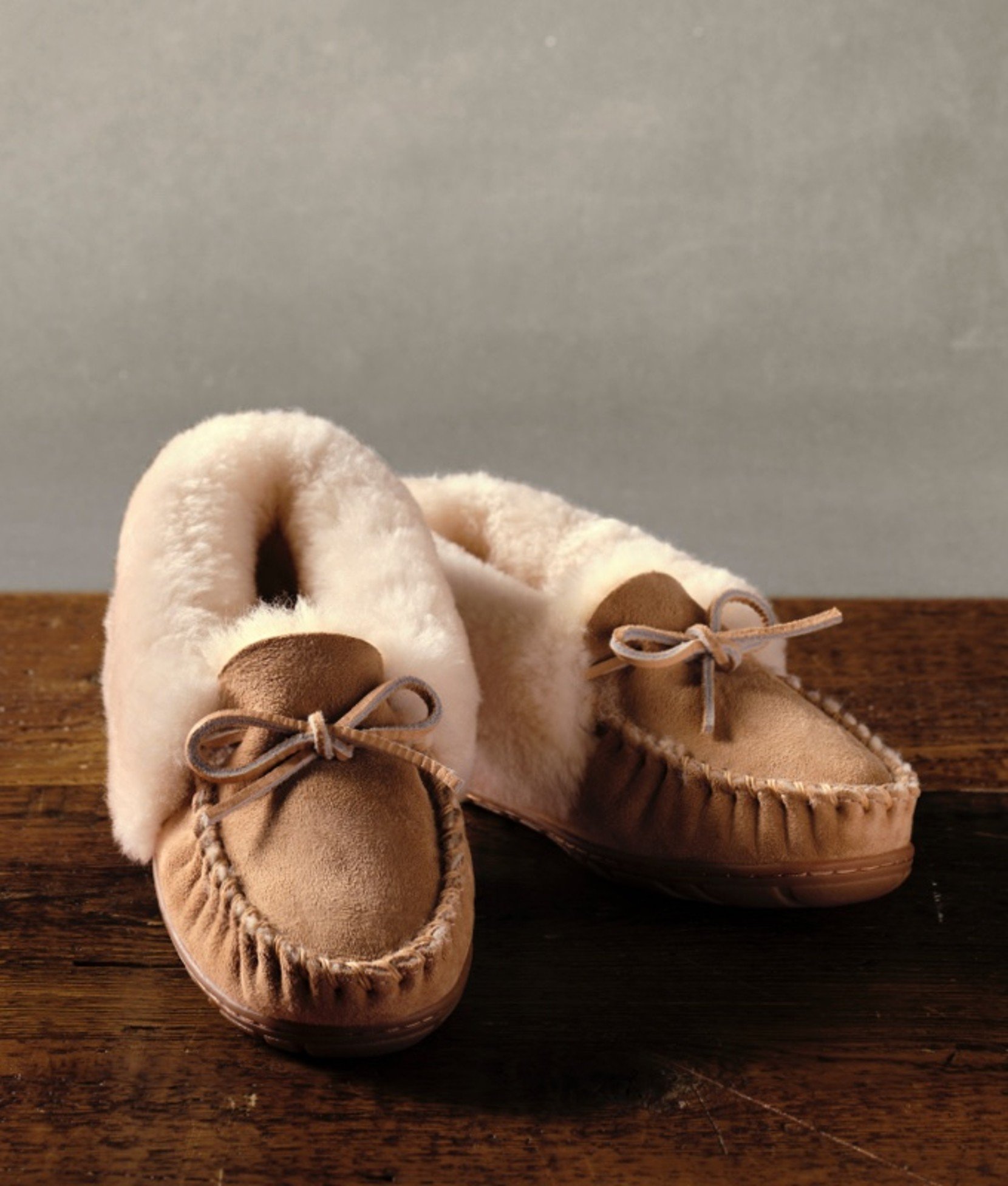 Tan moccasin slippers for women on a wooden surface. 