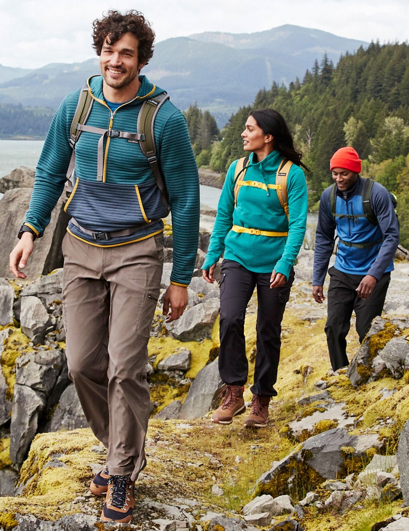 3 friends hiking on a rocky trail overlooking water, mountains in the background.