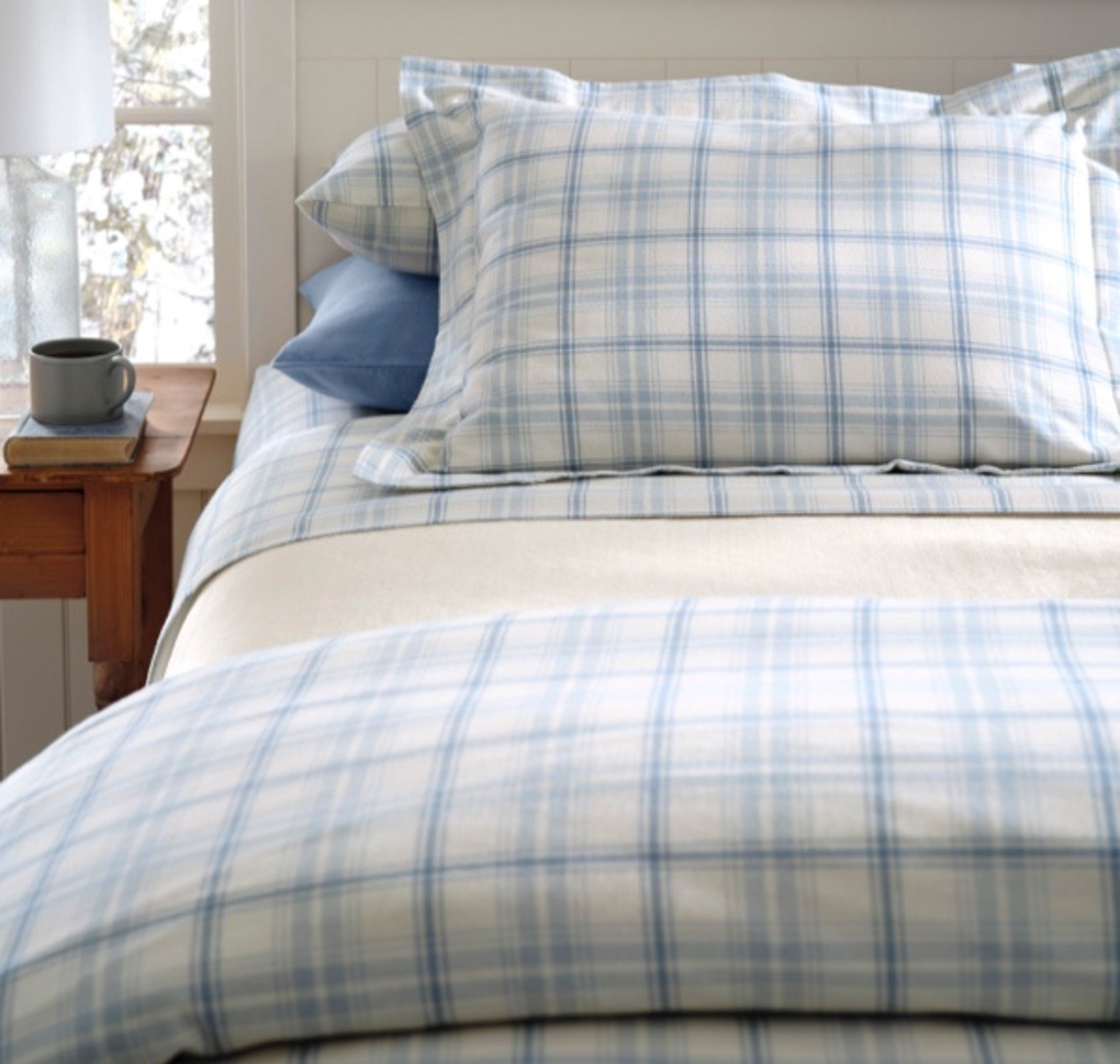 Light blue plaid flannel sheets on a bed in a cozy, softly lit room.