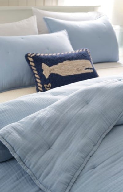 Light blue bedding set with matching pillows and a navy accent pillow featuring a whale design adds a coastal touch.