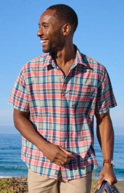 Person wearing a short‑sleeve plaid button‑up shirt and khaki pants while standing near the ocean.