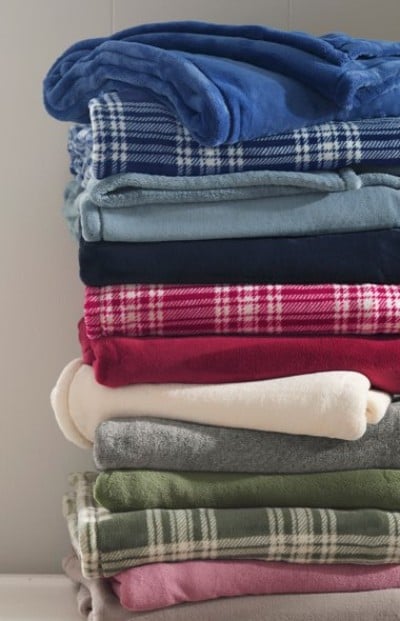 A tall stack of soft, folded blankets stacked neatly in assorted colors and plaid patterns.