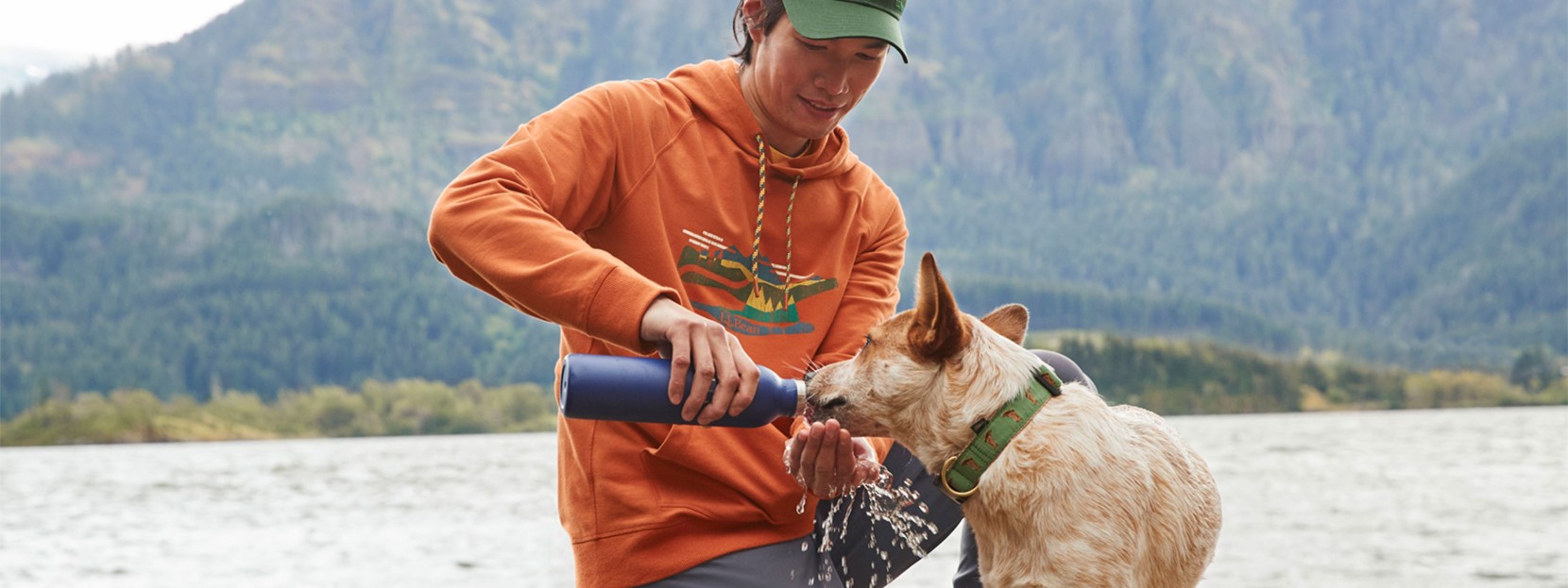 Someone on a dock giving a dog water out of their water bottle with a mountain and lake in the background.