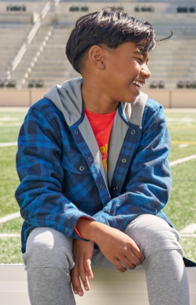 A boy sits on a bench at a sports field with a L L Bean backpack beside them.